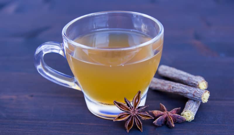 Taza de infusión con anís estrellado y raíces de regaliz apoyada sobre mesa oscura, ingredientes usados en remedios caseros para la tos.