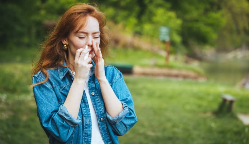 Mujer joven usando un spray nasal al aire libre, con signos de congestión y estornudos relacionados con rinitis no alérgica