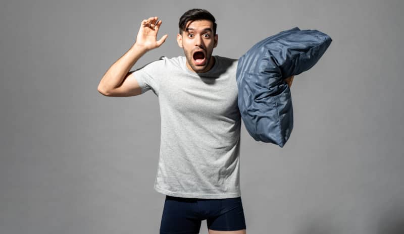 Hombre con almohada expresando un sobresalto debido a las alteraciones del sueño por sonambulismo