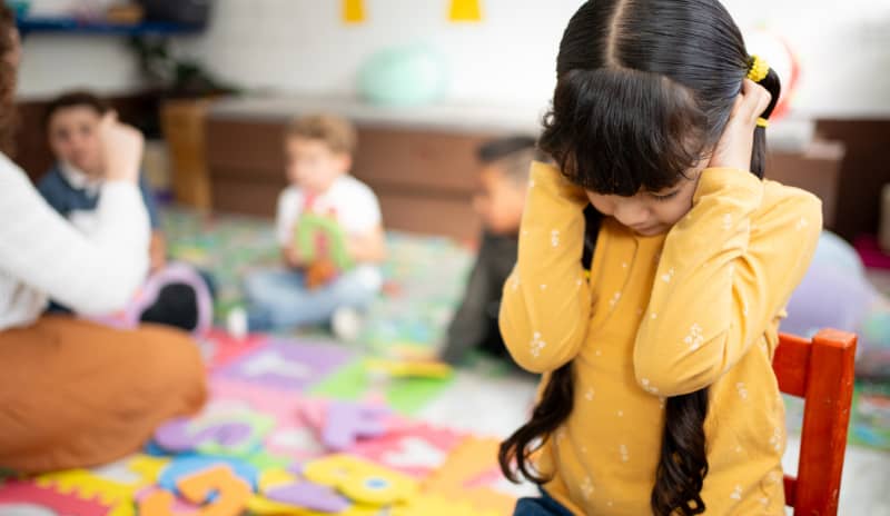 Niña pequeña tapándose los oídos en mitad de la clase como seña del autismo
