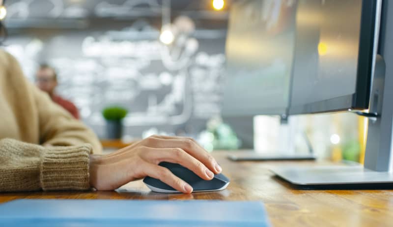 Persona utilizando el ratón del ordenador, en representación de la gestión de un trámite como cambiar de médico de cabecera.
