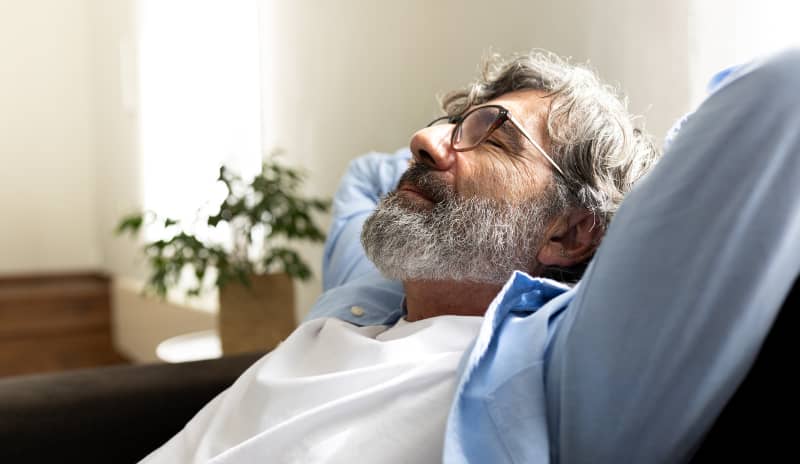Hombre reposando en el sofá con los brazos detrás de la cabeza y con los ojos cerrados en un momento de hormigueo en la cara