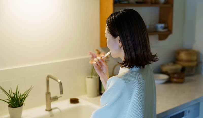 Mujer de espaldas cepillándose los dientes frente al lavabo, rutina diaria de lavarse los dientes.