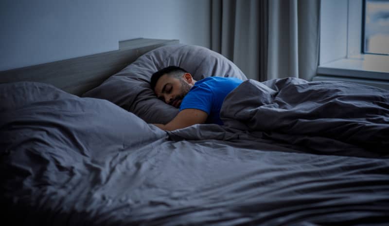 Hombre durmiendo boca abajo en su cama con la posibilidad de soñar con una persona fallecida