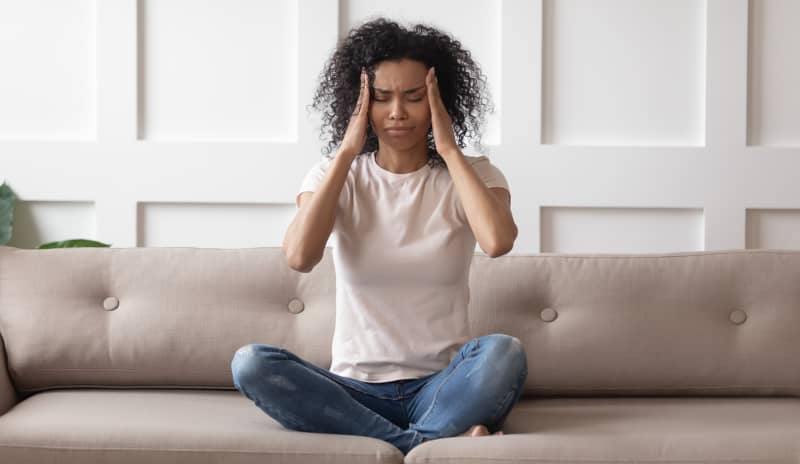 Mujer sentada en un sofá con expresión de malestar y las manos en la cabeza, mostrando síntomas comunes de un desequilibrio hormonal como dolores de cabeza o cambios de humor