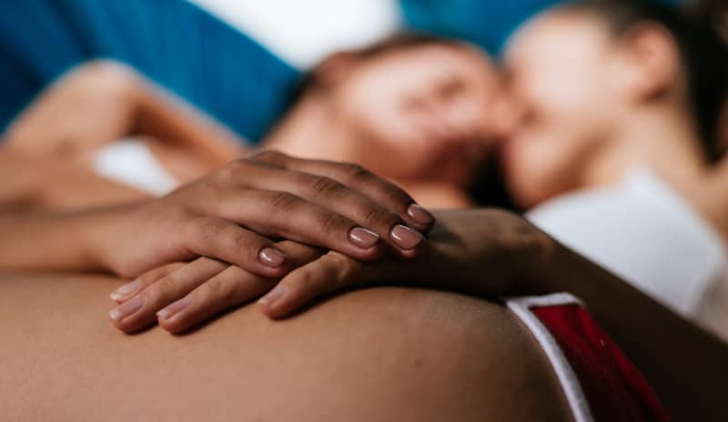 Primer plano de una pareja abrazada en la cama, con enfoque en el contacto físico y la intimidad, ilustrando deseo sexual y libido femenina en un contexto de conexión emocional y afectiva