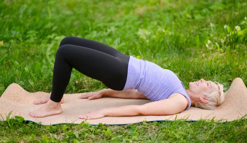 Mujer realizando un ejercicio de puente de glúteos sobre una esterilla al aire libre, una práctica habitual para aliviar y prevenir el dolor de espalda baja fortaleciendo la zona lumbar