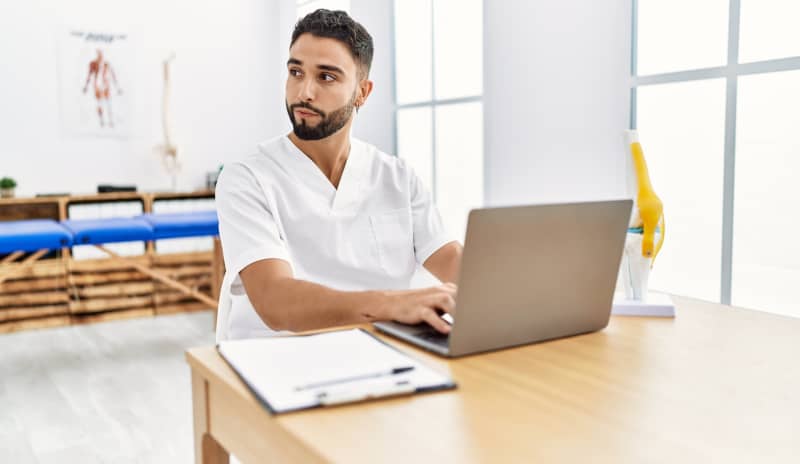 Fisioterapeuta sentado frente a un ordenador en una consulta, analizando información médica relacionada con lesiones en corredores