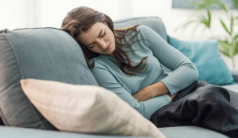 Mujer recostada en el sofá con expresión de malestar y la mano en el abdomen, asociado a dolor de vientre bajo sin menstruación
