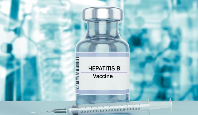 Vial con la etiqueta “Hepatitis B Vaccine” junto a una jeringa, con un fondo de laboratorio desenfocado