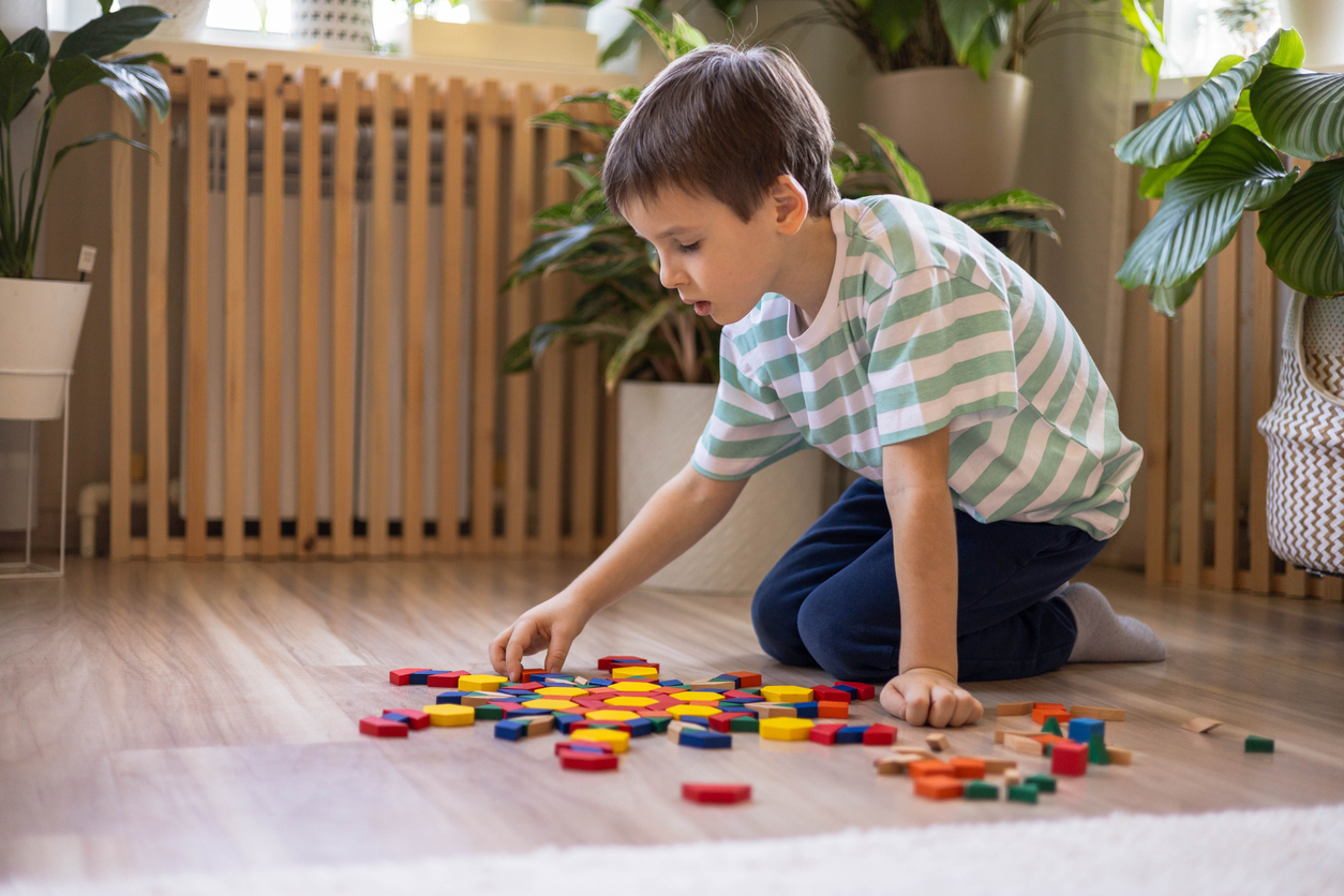Niño pequeño jugando en el suelo con piezas de colores, concentrado en ordenar y clasificar los bloques, imagen representativa del autismo y de actividades que estimulan la atención y el desarrollo cognitivo