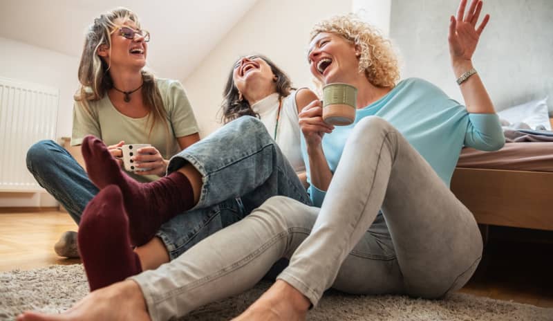 Grupo de amigas riendo y conversando sentadas en el suelo tomando café sin móviles a la vista, mostrando los beneficios de la desconexión digital frente a la nomofobia