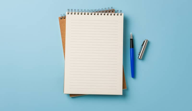 Cuaderno de espiral abierto con páginas en blanco y un bolígrafo azul sobre fondo claro, listos para empezar una práctica de journaling terapéutico.