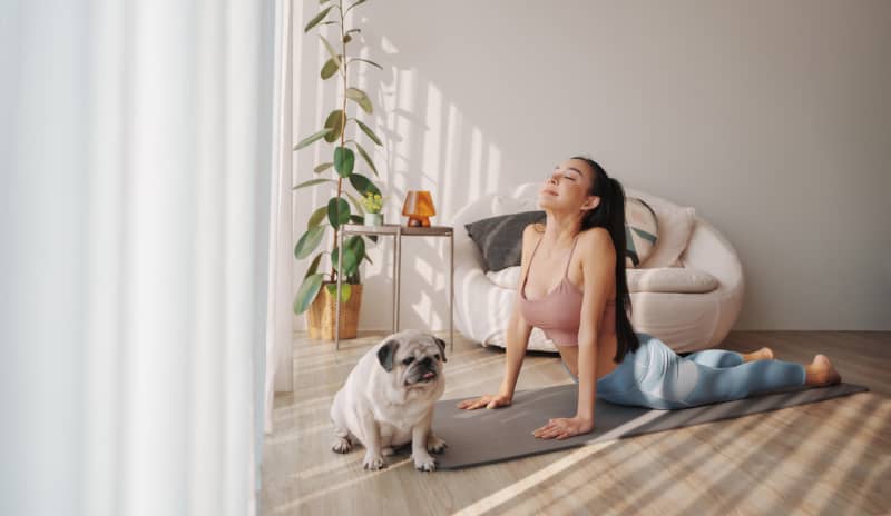 Mujer joven practicando una postura de yoga sobre una esterilla en el salón de su casa con luz natural, como ejemplo de microhábitos de movimiento en la rutina diaria