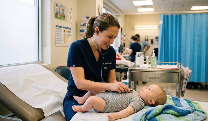 Pediatra examinando con estetoscopio a un bebé tumbado en una camilla en urgencias pediátricas por bronquilitis