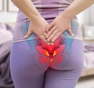 Mujer de espaldas tocándose la parte baja de la espalda con una ilustración sobre el área del coxis destacada en rojo, representando el dolor de coxis sin golpe