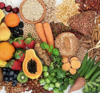 Variedad de frutas, verduras, legumbres, cereales integrales y frutos secos sobre fondo claro, ejemplos de alimentos ricos en fibra.