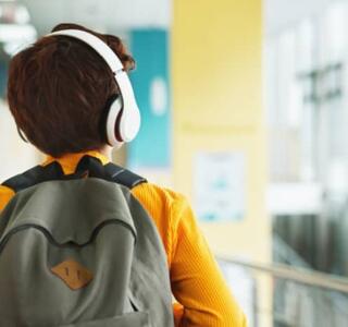 Niño de espaldas con mochila y auriculares caminando por un pasillo escolar, relacionado con el síndrome de Asperger.