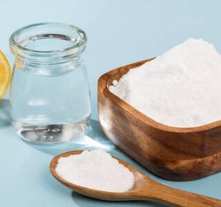 Un cuenco y una cuchara de madera llenos de bicarbonato, un vaso con agua y medio limón, ingredientes utilizados en remedios caseros para la tos.