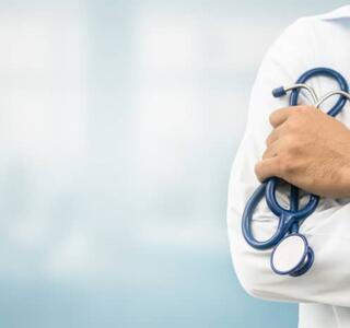 Torso de un médico con bata blanca sosteniendo un estetoscopio sobre un fondo difuminado, simbolizando la atención sanitaria y el proceso de cambiar de médico de cabecera.