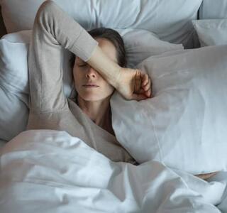 Mujer acostada en la cama con el brazo sobre los ojos, imagen asociada al malestar provocado por la cefalea tensional crónica.