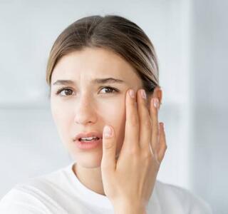 Mujer joven tocándose la mejilla con expresión de preocupación, representando la sensación de hormigueo en la cara y su posible causa