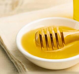 Cuenco con miel con su utensilio de madera para servir, alimento que debe evitarse en casos de intolerancia a la fructosa.