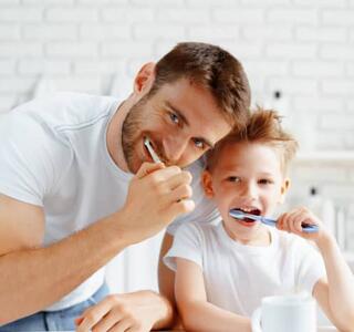 Padre e hijo en la rutina habitual de lavarse los dientes frente al espejo, hábito diario de higiene bucal.