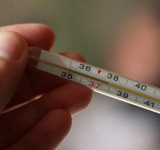 Mano sosteniendo un termómetro con escala visible en grados centígrados, usado para medir la temperatura corporal.