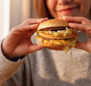 Mujer sosteniendo una hamburguesa con queso y lechuga antes de comérsela, representando un ejemplo claro de alimentos ultraprocesados con alto contenido en grasas y aditivos