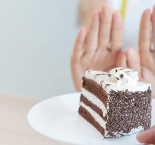 Imagen de un trozo de pastel en un plato y detrás las manos de alguien haciendo un gesto rechazándolo, representando alimentos prohibidos para la dispepsia