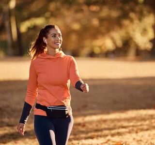 Mujer caminando al aire libre por un parque en otoño con ropa deportiva, imagen que representa los beneficios de caminar para la salud física y el bienestar mental