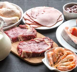 Alimentos ricos en proteínas como carne, pollo, salmón, gambas, huevos y lácteos dispuestos sobre una mesa, todos representativos de la dieta Dukan basada en el consumo de proteínas animales