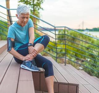 Mujer corredora sentada en unas escaleras sujetándose el tobillo con gesto de dolor, mostrando un posible caso de lesiones en corredores