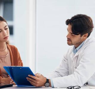 Mujer joven en consulta médica revisando resultados con un profesional sanitario, en el contexto del diagnóstico de menopausia precoz.