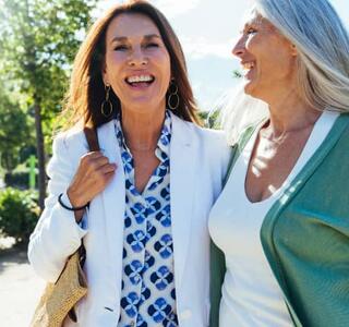 Dos mujeres maduras riendo y paseando juntas al aire libre en un parque con luz natural