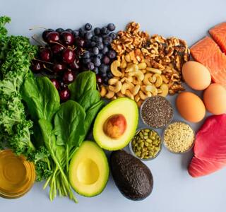 Vista cenital de alimentos antiinflamatorios como salmón, atún, kale, espinacas, aguacate, arándanos, nueces, semillas, huevos y aceite de oliva sobre fondo claro