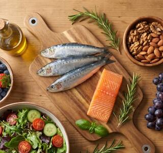 Sardinas, salmón, frutos rojos, uvas, frutos secos, ensalada y aceite de oliva sobre una mesa de madera en representación de alimentos que forman parte del patrón de la nutrición antiedad.