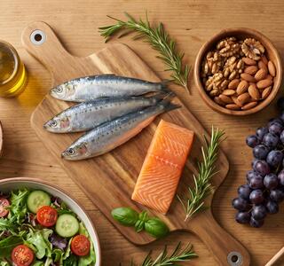 Sardinas, salmón, frutos rojos, uvas, frutos secos, ensalada y aceite de oliva sobre una mesa de madera en representación de alimentos que forman parte del patrón de la nutrición antiedad.
