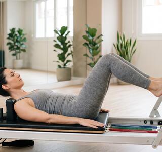 Mujer haciendo footwork en una máquina de pilates reformer en una sala específica para esta actividad, en representación de la comparativa de pilates reformer vs mat