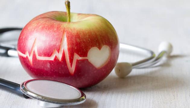 Manzana roja con dibujo de corazón y electrocardiograma ejemplifica el colesterol bueno y malo