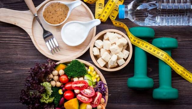 Imagen cenital de un plato de verduras, botella de agua, pesas y demás objetos que puedn ayudar a bajar 4 kilos en un mes