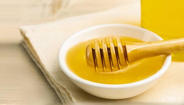 Cuenco con miel con su utensilio de madera para servir, alimento que debe evitarse en casos de intolerancia a la fructosa.