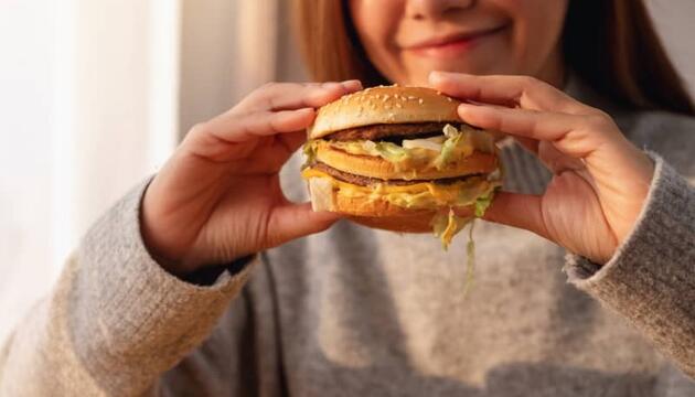 Mujer sosteniendo una hamburguesa con queso y lechuga antes de comérsela, representando un ejemplo claro de alimentos ultraprocesados con alto contenido en grasas y aditivos