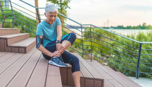 Mujer corredora sentada en unas escaleras sujetándose el tobillo con gesto de dolor, mostrando un posible caso de lesiones en corredores