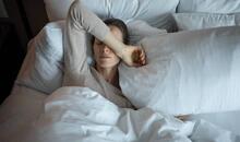 Mujer acostada en la cama con el brazo sobre los ojos, imagen asociada al malestar provocado por la cefalea tensional crónica.