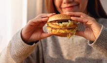 Mujer sosteniendo una hamburguesa con queso y lechuga antes de comérsela, representando un ejemplo claro de alimentos ultraprocesados con alto contenido en grasas y aditivos