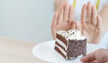 Imagen de un trozo de pastel en un plato y detrás las manos de alguien haciendo un gesto rechazándolo, representando alimentos prohibidos para la dispepsia