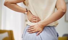 Mujer sosteniendo la zona lumbar con ambas manos, mostrando molestias típicas del dolor de espalda baja