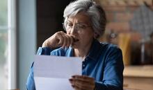Mujer mayor con gafas leyendo un documento con gesto de preocupación en su cocina, reflejando la ansiedad financiera que generan las facturas y notificaciones económicas
